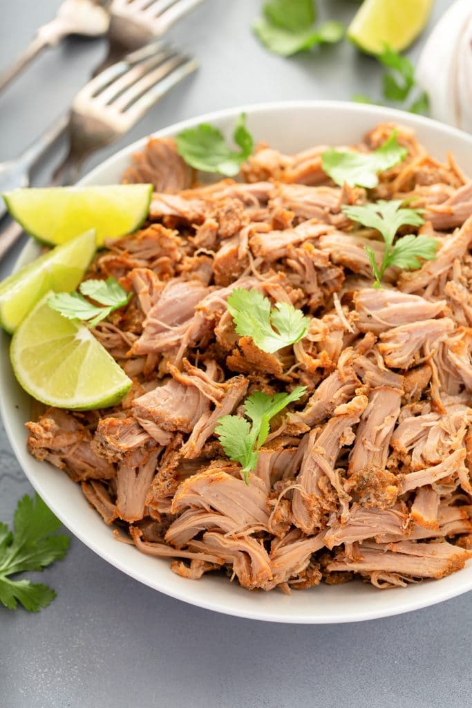 Pork carnitas in a bowl with celery and lime wedges