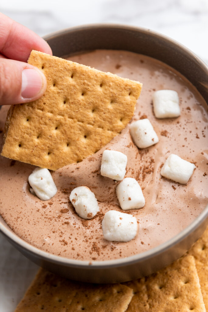scooping hot cocoa dip onto a graham cracker
